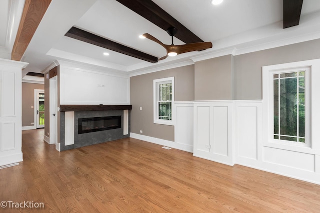 unfurnished living room with ceiling fan, beamed ceiling, ornamental molding, and light wood-type flooring