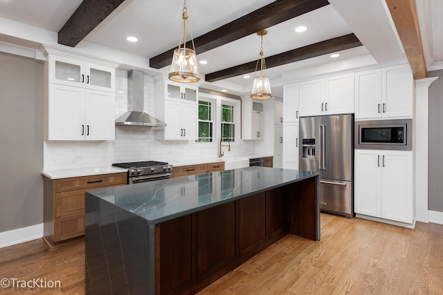 kitchen featuring premium appliances, a kitchen island, wall chimney range hood, beam ceiling, and white cabinetry