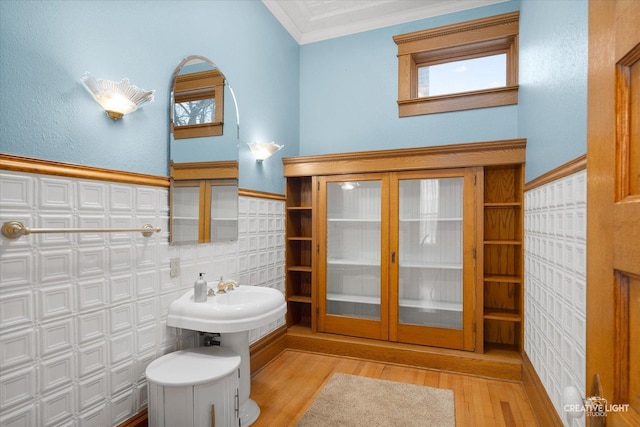 bathroom featuring hardwood / wood-style flooring, a wealth of natural light, ornamental molding, and tile walls