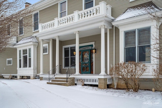 snow covered property entrance with a balcony