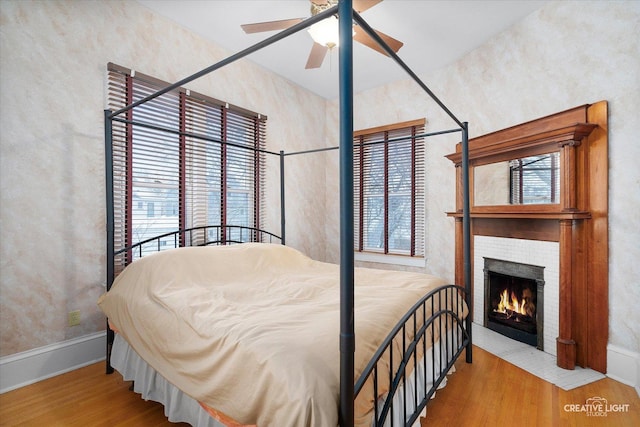 bedroom with a fireplace, light hardwood / wood-style floors, and ceiling fan