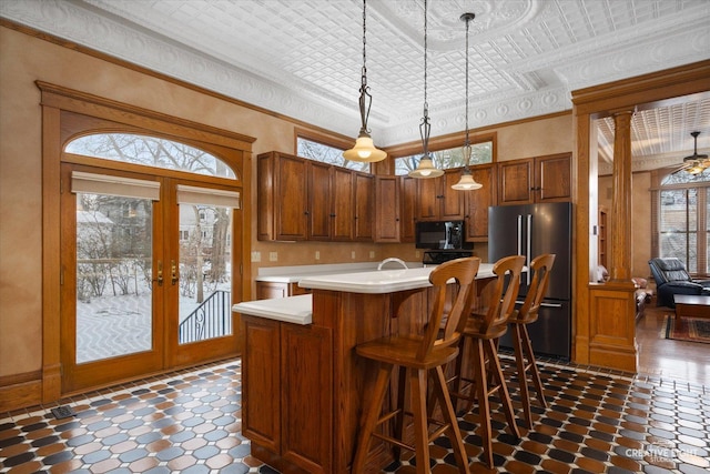 kitchen featuring stainless steel fridge, french doors, hanging light fixtures, a breakfast bar area, and an island with sink