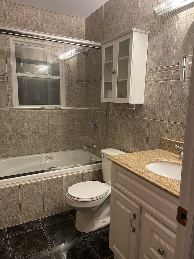 full bathroom with vanity, toilet, bath / shower combo with glass door, and tile walls