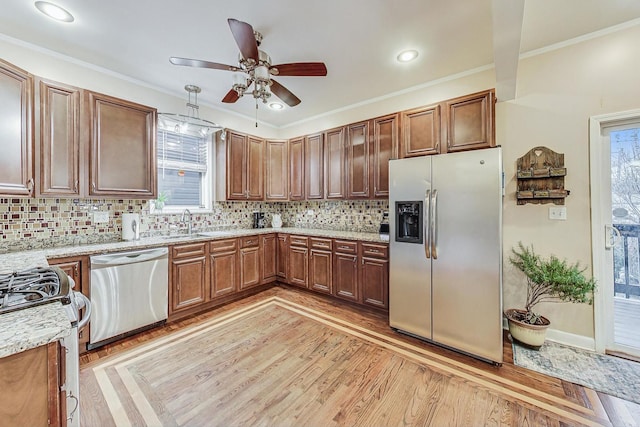 kitchen featuring decorative backsplash, appliances with stainless steel finishes, ornamental molding, ceiling fan, and light hardwood / wood-style floors