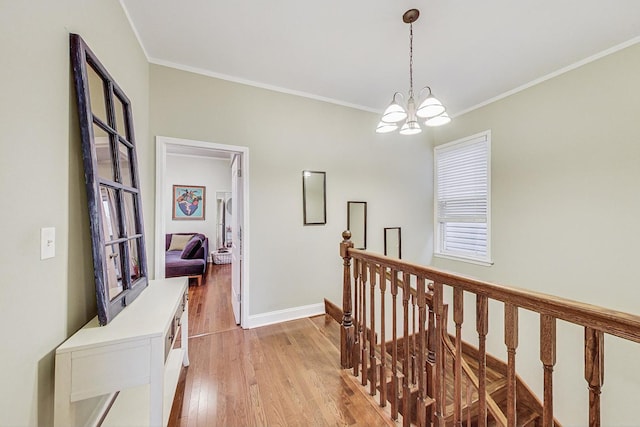 hallway with light wood-type flooring, an inviting chandelier, and ornamental molding