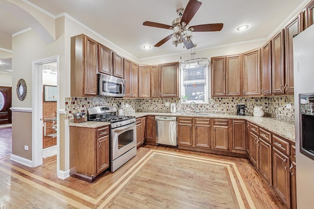 kitchen with sink, light hardwood / wood-style flooring, backsplash, crown molding, and appliances with stainless steel finishes