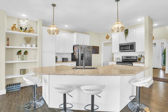 kitchen featuring an island with sink, white cabinets, stainless steel appliances, and decorative light fixtures