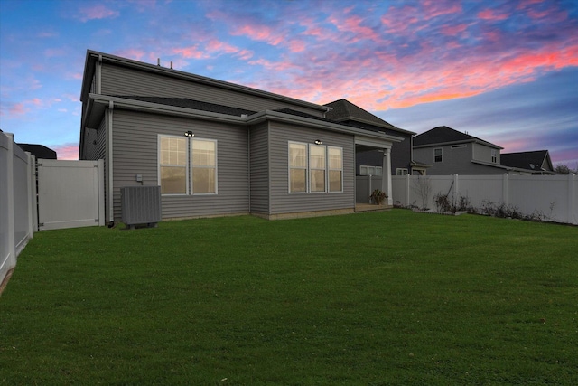 back house at dusk featuring a lawn and central air condition unit