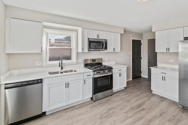 kitchen with sink, white cabinets, stainless steel appliances, and light hardwood / wood-style floors