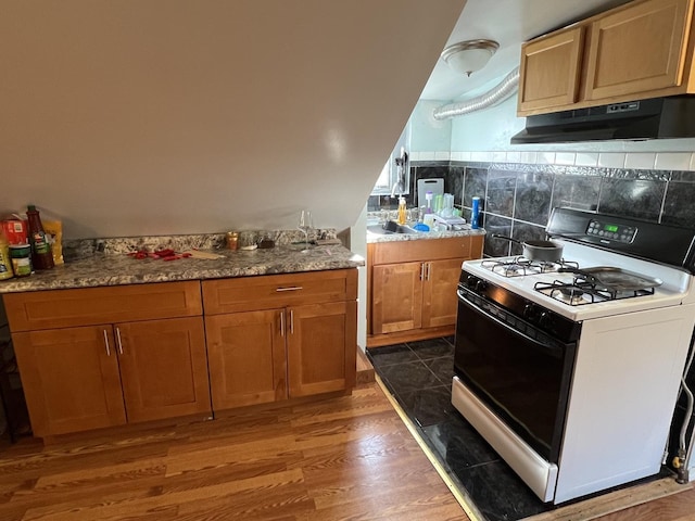 kitchen with backsplash, white gas stove, light stone counters, and dark wood-type flooring