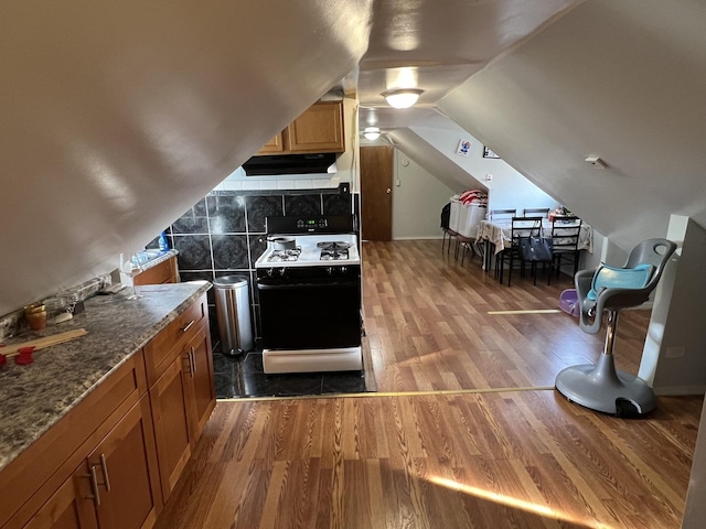 kitchen featuring lofted ceiling, dark stone counters, white range with gas stovetop, ventilation hood, and wood-type flooring