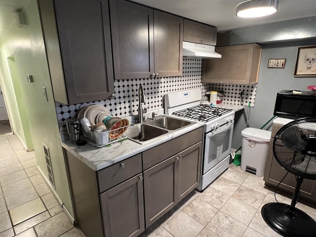 kitchen with sink, stainless steel gas range, light tile patterned floors, tasteful backsplash, and extractor fan