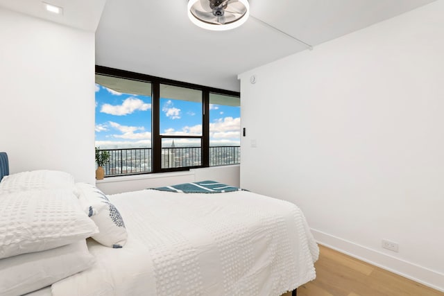 bedroom with ceiling fan, a wall of windows, and light wood-type flooring