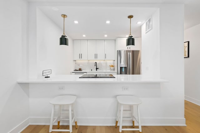 kitchen with stainless steel refrigerator with ice dispenser, decorative light fixtures, white cabinetry, and light hardwood / wood-style floors