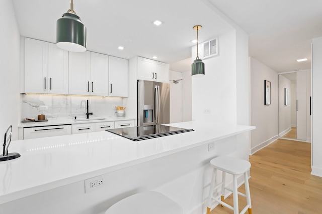 kitchen featuring a breakfast bar, sink, stainless steel refrigerator with ice dispenser, light hardwood / wood-style flooring, and white cabinetry