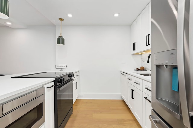 kitchen with light wood-type flooring, stainless steel appliances, white cabinetry, and hanging light fixtures