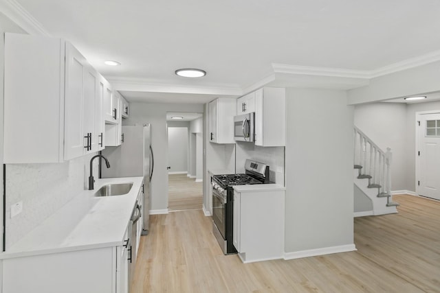 kitchen with sink, stainless steel appliances, crown molding, white cabinets, and light wood-type flooring