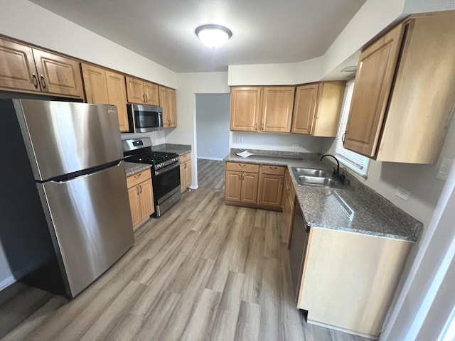 kitchen with dark stone countertops, sink, stainless steel appliances, and light wood-type flooring