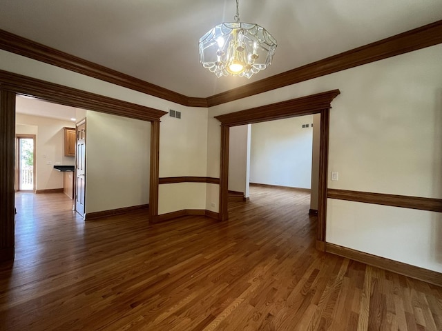 unfurnished room with ornamental molding, dark wood-type flooring, and an inviting chandelier