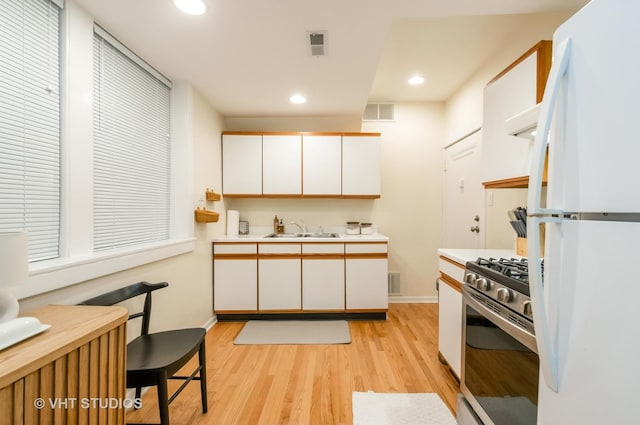 kitchen with a sink, light wood-style floors, light countertops, freestanding refrigerator, and gas range