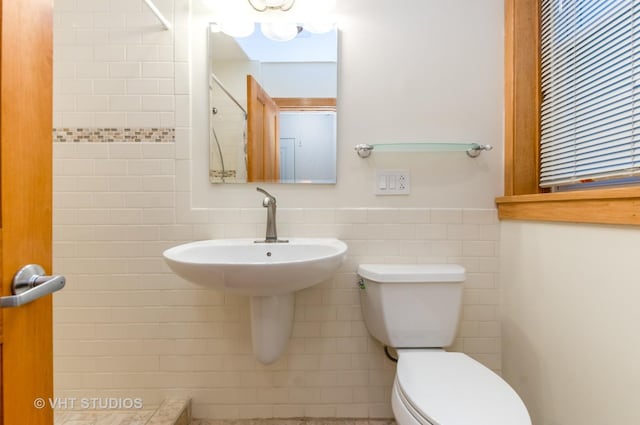 bathroom featuring toilet, wainscoting, a sink, and tile walls