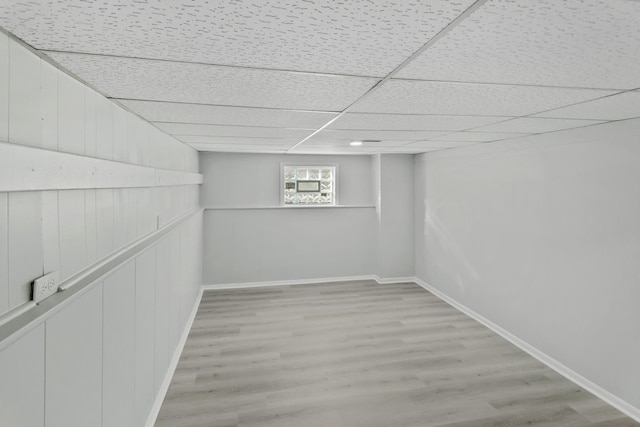 basement with light wood-type flooring and a paneled ceiling