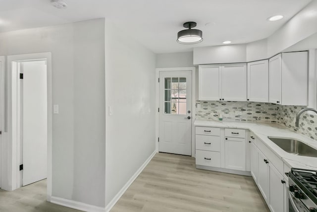 kitchen featuring sink, light stone counters, tasteful backsplash, light hardwood / wood-style floors, and white cabinets