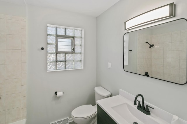 bathroom with a tile shower, vanity, and toilet