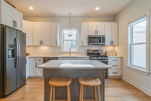 kitchen with pendant lighting, white cabinets, sink, appliances with stainless steel finishes, and light hardwood / wood-style floors