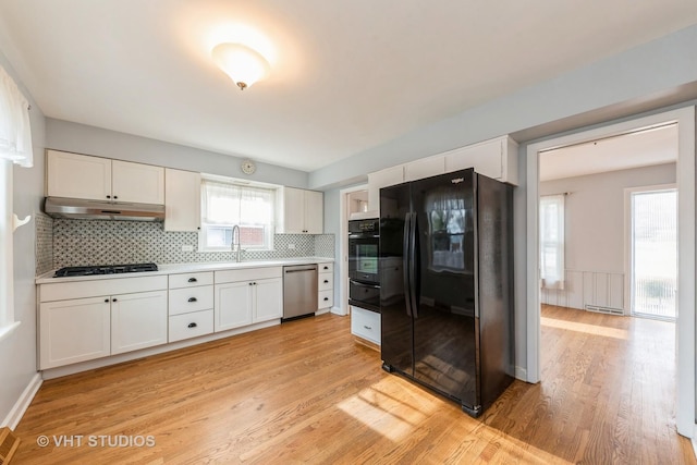 kitchen with backsplash, black fridge, stainless steel dishwasher, white cabinets, and light hardwood / wood-style floors