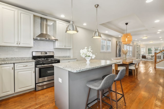 kitchen with wall chimney exhaust hood, a tray ceiling, white cabinets, a kitchen island, and stainless steel range with gas stovetop