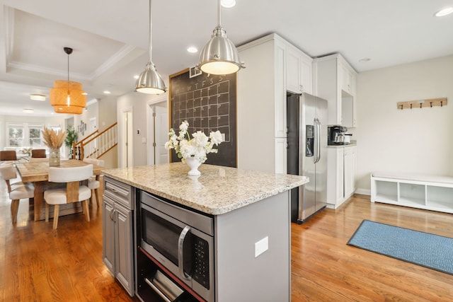 kitchen with hanging light fixtures, stainless steel appliances, a tray ceiling, white cabinets, and hardwood / wood-style flooring