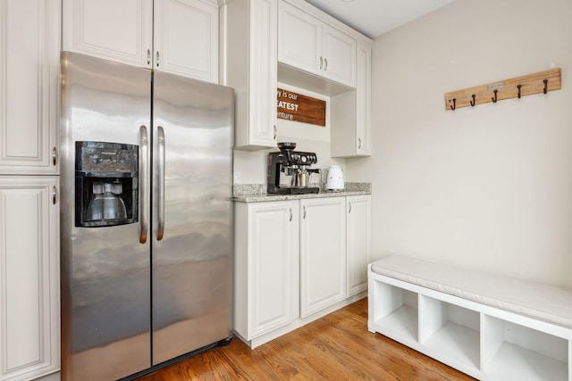 interior space with white cabinets, stainless steel refrigerator with ice dispenser, light hardwood / wood-style floors, and light stone countertops