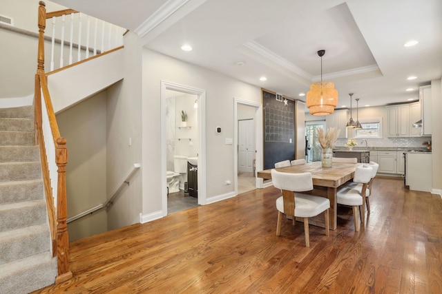 dining area with hardwood / wood-style floors, ornamental molding, sink, and a tray ceiling