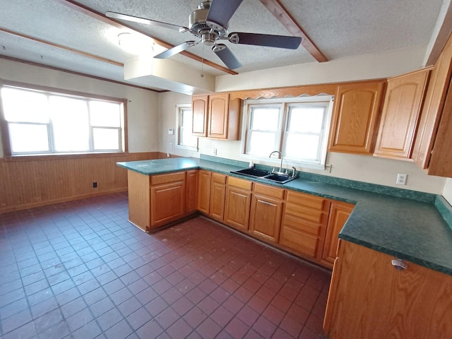 kitchen featuring a textured ceiling, ceiling fan, wood walls, and sink