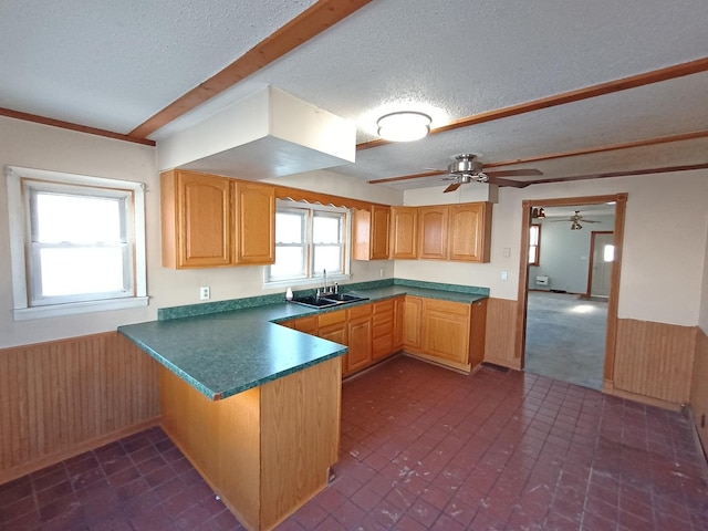 kitchen with ceiling fan, sink, kitchen peninsula, a textured ceiling, and wooden walls