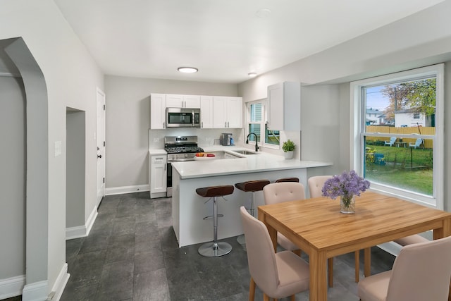 kitchen with sink, stainless steel appliances, kitchen peninsula, a breakfast bar, and white cabinets