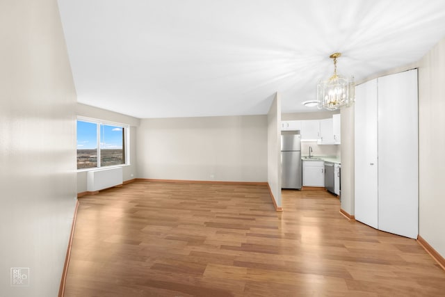 unfurnished living room featuring sink, a chandelier, and light wood-type flooring