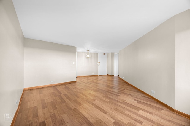 spare room with a notable chandelier and light wood-type flooring