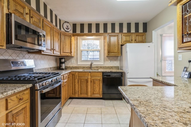 kitchen with decorative backsplash, appliances with stainless steel finishes, light stone counters, sink, and light tile patterned flooring