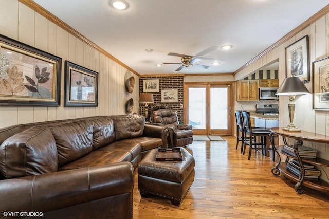 living room with crown molding, wooden walls, ceiling fan, and light hardwood / wood-style floors