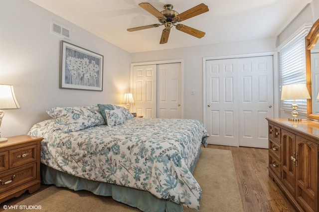 bedroom featuring two closets, light hardwood / wood-style floors, and ceiling fan