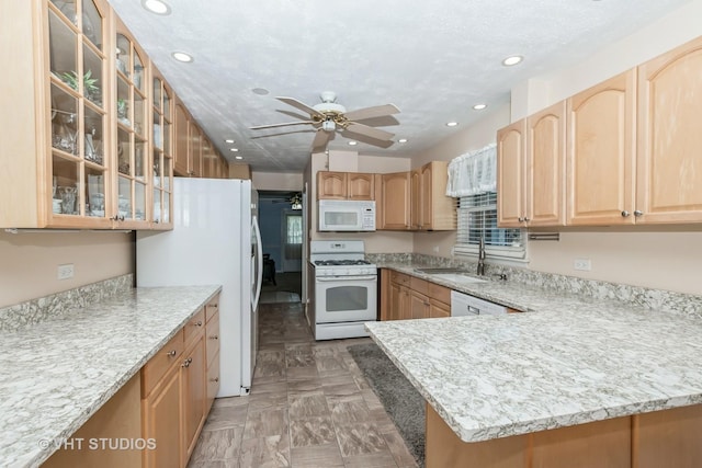 kitchen with kitchen peninsula, light stone countertops, white appliances, ceiling fan, and sink