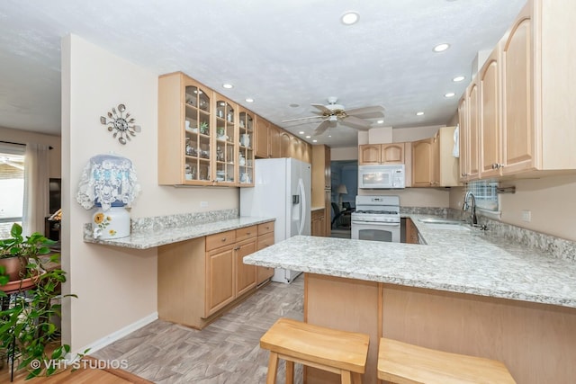 kitchen with a breakfast bar, white appliances, sink, light stone counters, and kitchen peninsula