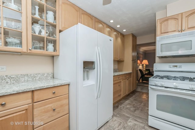 kitchen with light stone counters, light brown cabinets, and white appliances