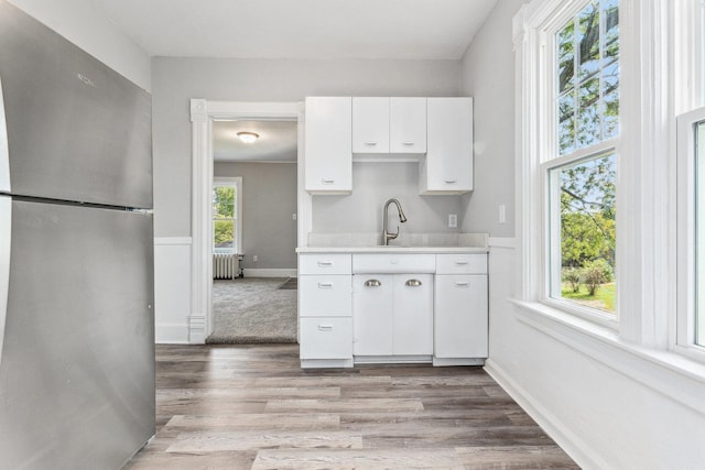 kitchen featuring stainless steel fridge, radiator heating unit, white cabinetry, and a wealth of natural light