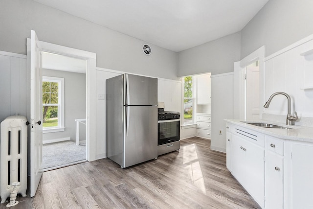 kitchen with white cabinets, sink, light hardwood / wood-style floors, radiator heating unit, and stainless steel appliances