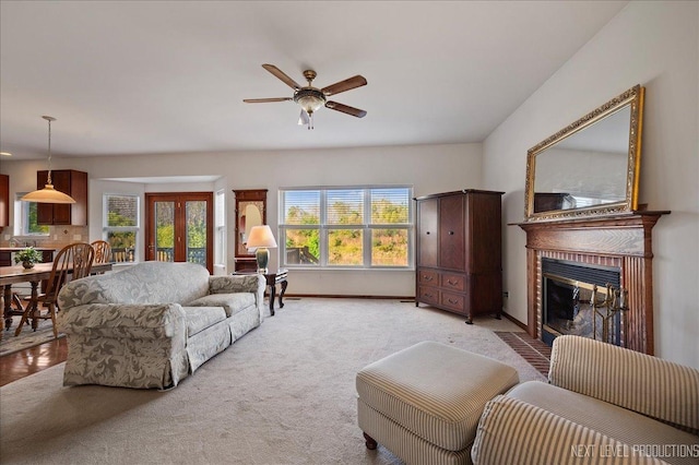 living area featuring light colored carpet, a brick fireplace, baseboards, and ceiling fan