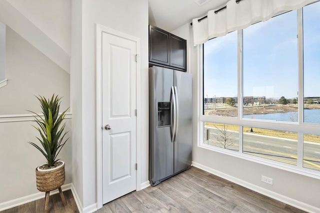 kitchen with stainless steel fridge, a water view, and light wood-type flooring