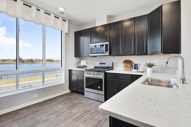 kitchen with sink, a water view, stainless steel appliances, and light hardwood / wood-style flooring